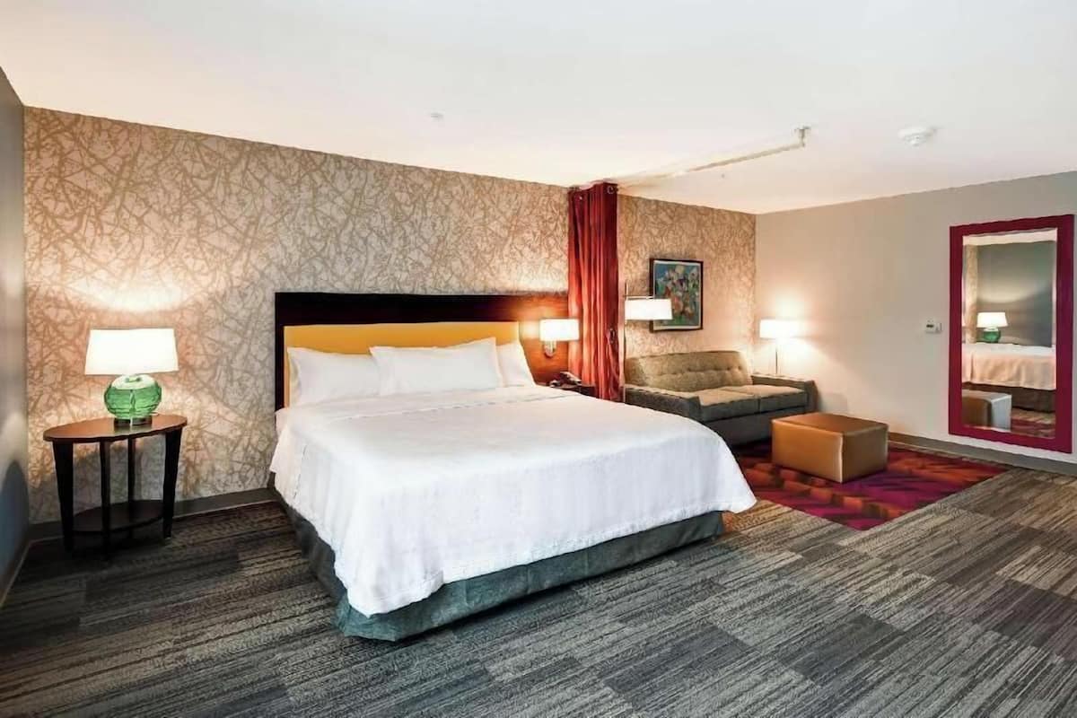 A hotel room with a large bed, a sofa, a small table, and a mirror.