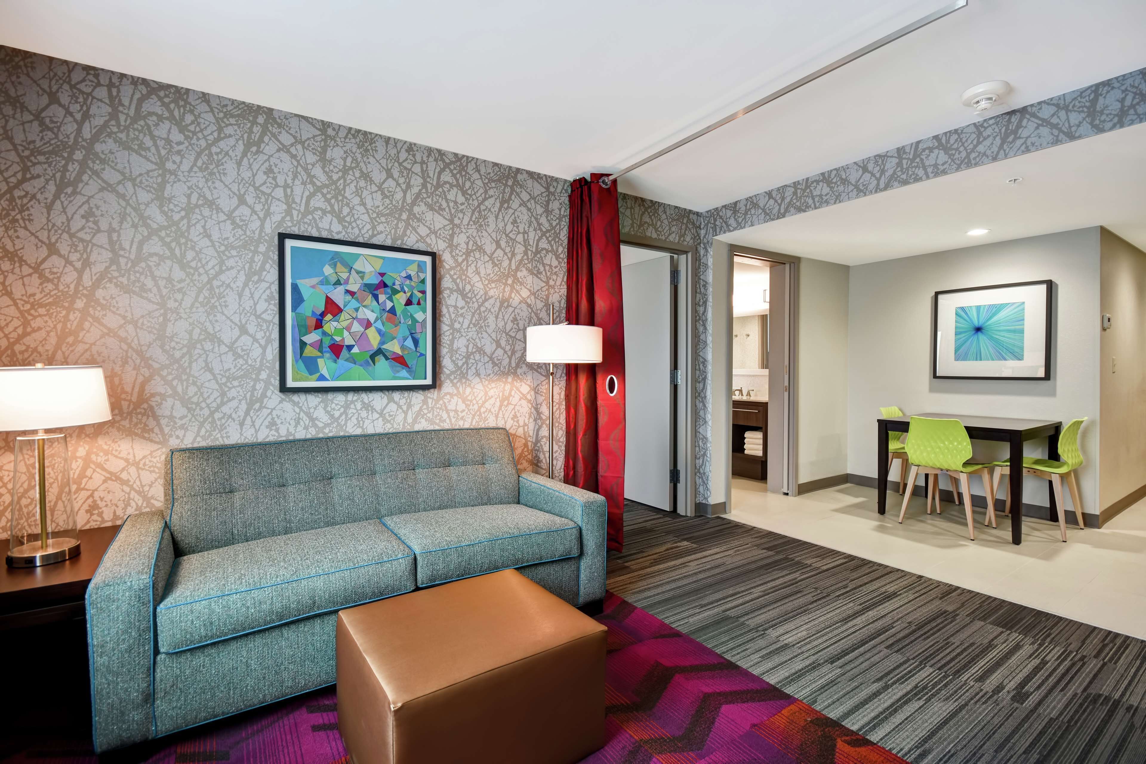 A hotel room with a sofa, a table with chairs, a lamp, and artwork on the walls.