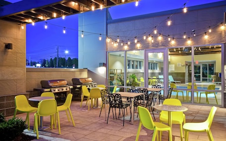 An outdoor patio with yellow chairs and tables, a barbecue grill, and string lights.