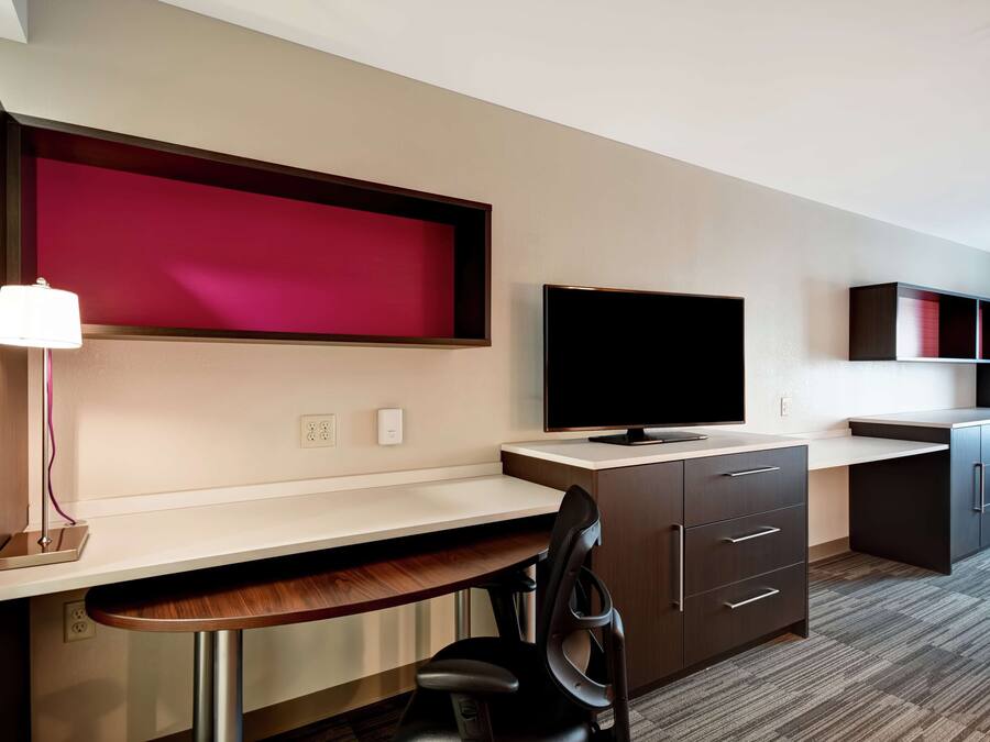 A modern hotel room with a desk, chair, flat-screen TV, and built-in cabinets.