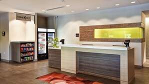 A reception area with a counter, a refrigerator stocked with beverages, and a snack shelf. - Home2 Suites by Hilton Walpole Foxboro (Walpole)