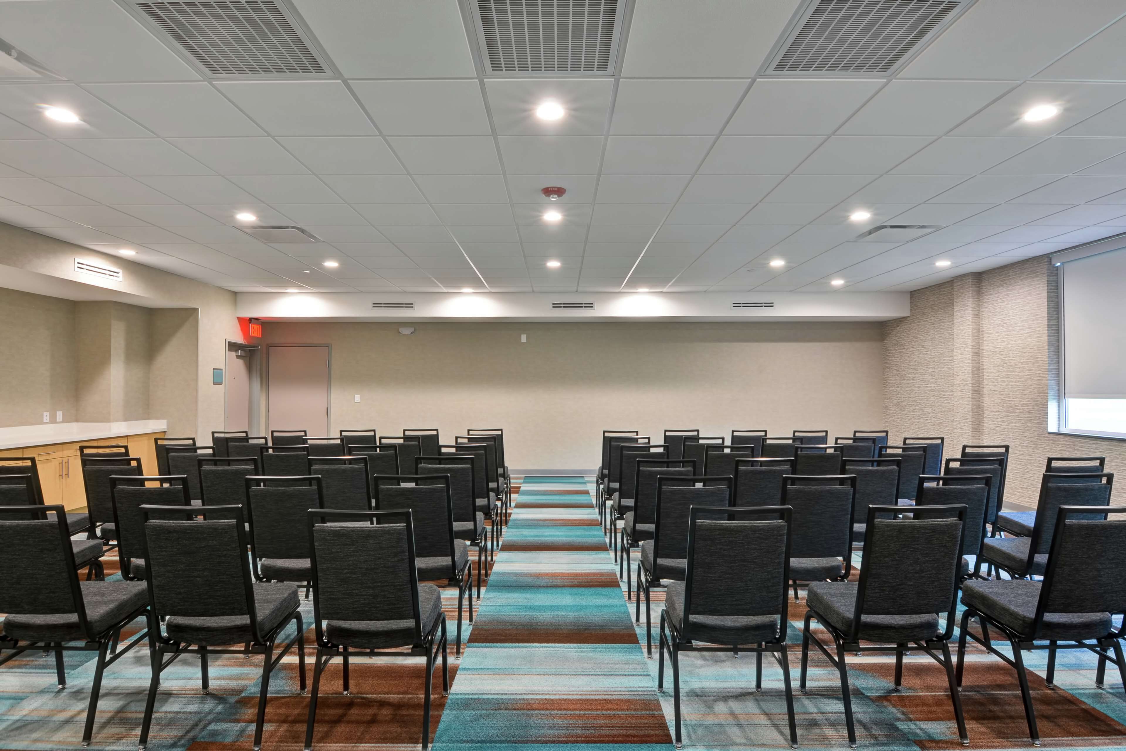 A conference room with rows of chairs, a carpeted floor, and a projector screen on the wall.