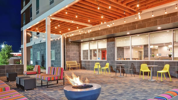 An outdoor seating area with a fire feature, yellow chairs, and a modern building facade. - Home2 Suites by Hilton La Porte (La Porte)