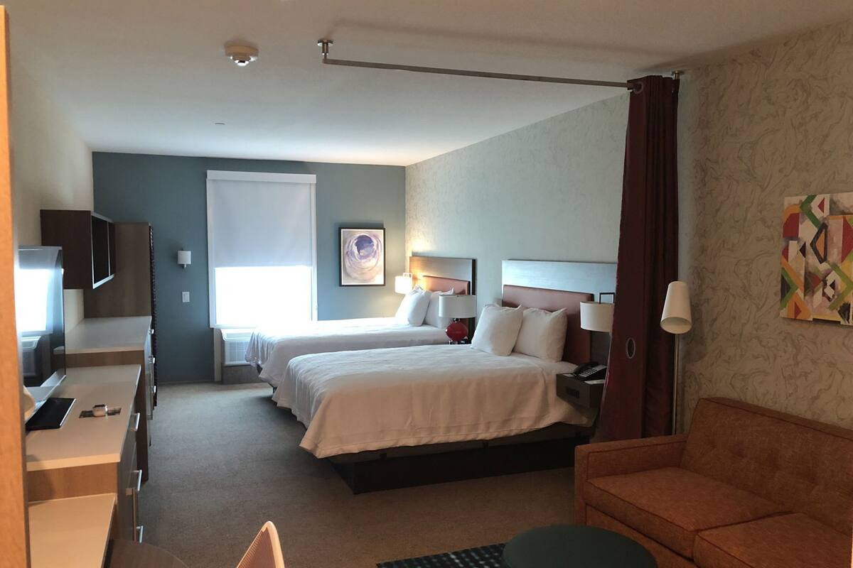 Een hotelkamer met een bed, twee nachtkastjes, een bureau met stoel, een televisie en een raam met gordijnen.
