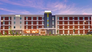 A multi-story hotel with a central tower, multiple windows, and a well-maintained lawn in front. - Home2 Suites by Hilton La Porte (La Porte)