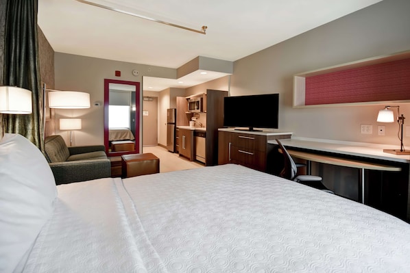 Una habitación de hotel con una cama grande, un escritorio, televisor, kitchenette y un espejo.