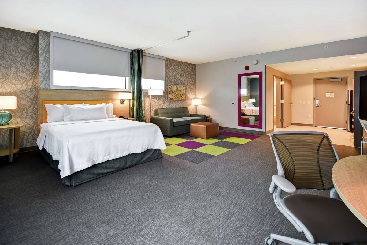 A hotel room with a bed, a desk, a chair, a sofa, and a bathroom door.