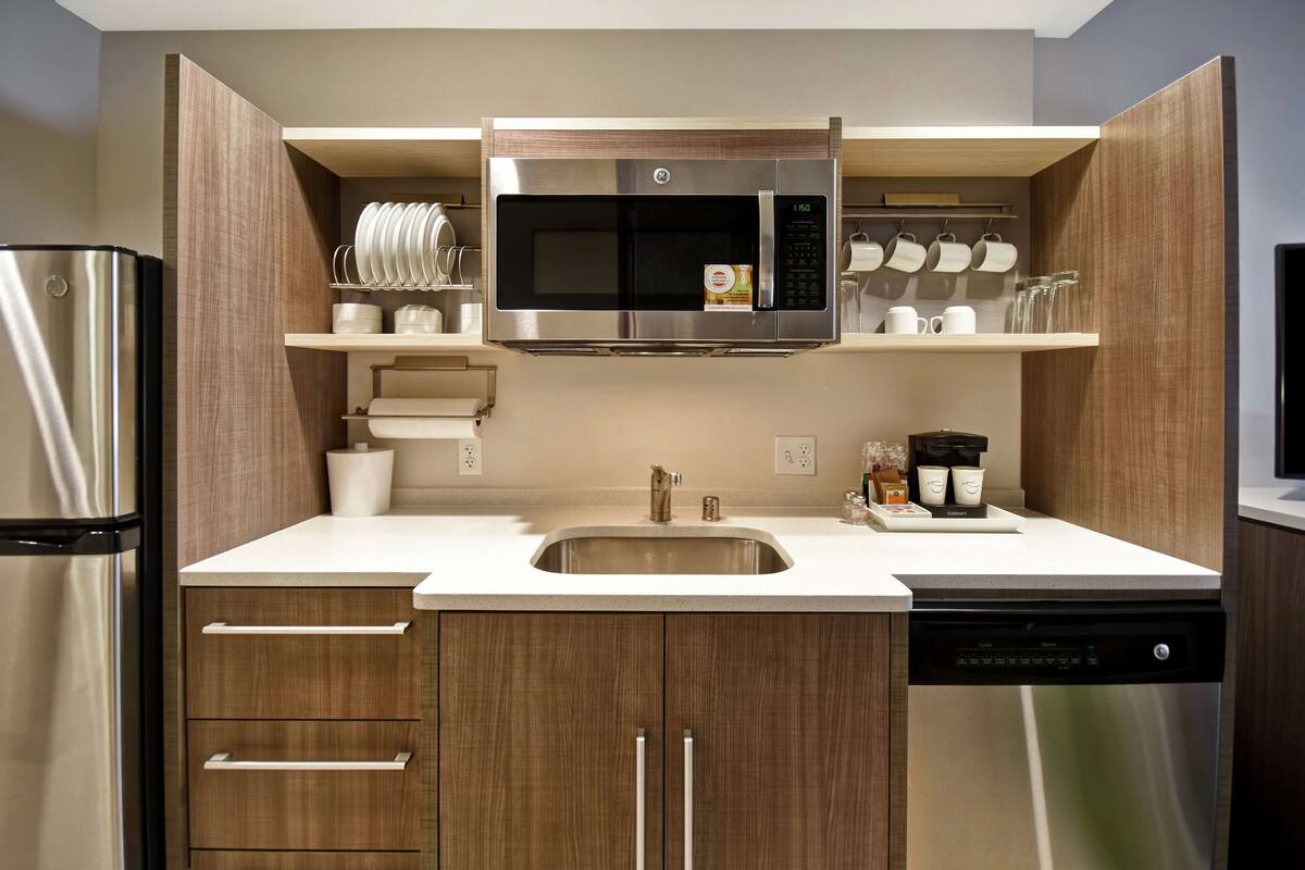A modern kitchen with a stainless steel refrigerator, a built-in microwave, a dishwasher, and wooden cabinets.