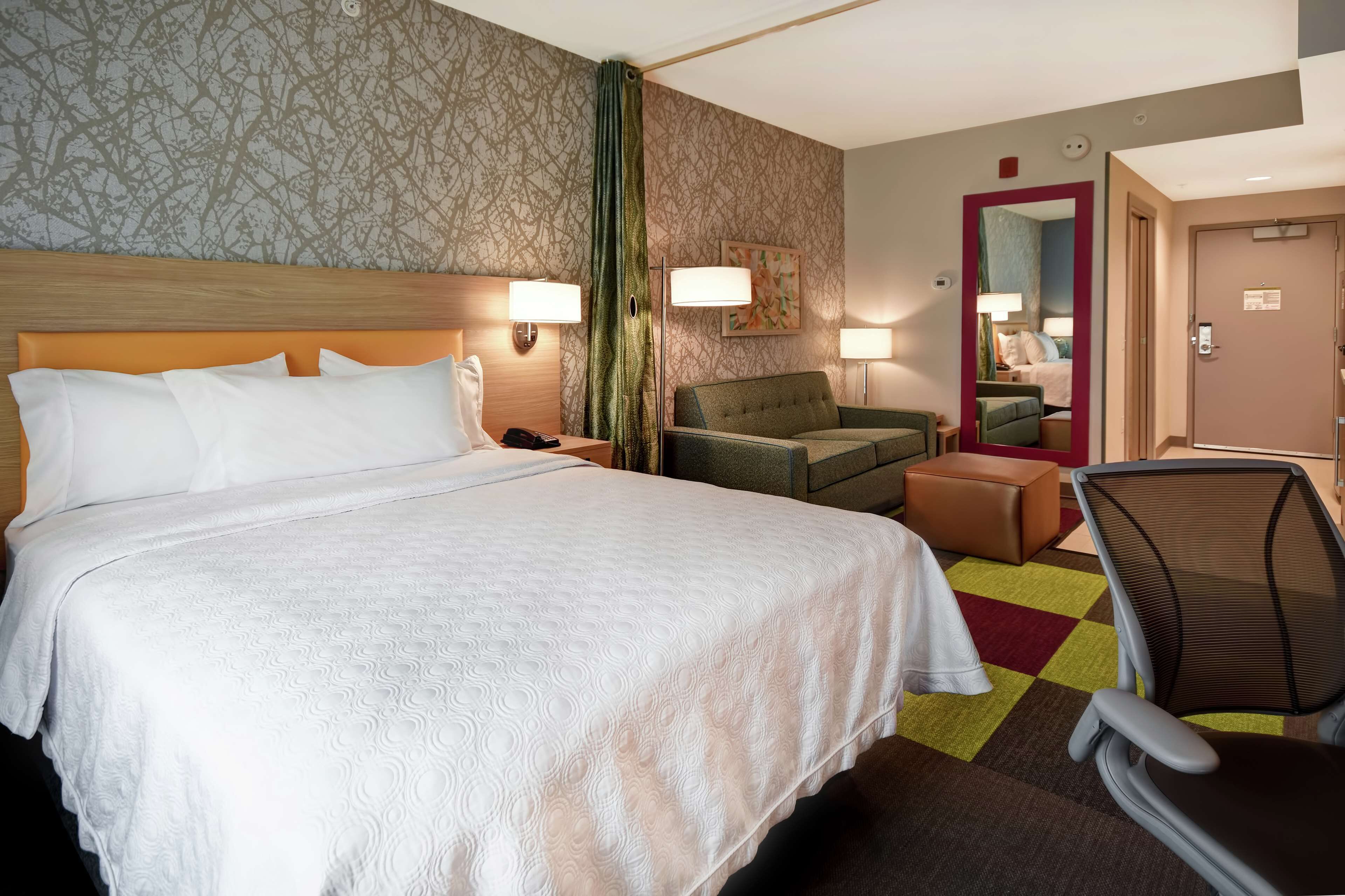 A hotel room with a large bed, a desk with a lamp, a chair, and a mirror.