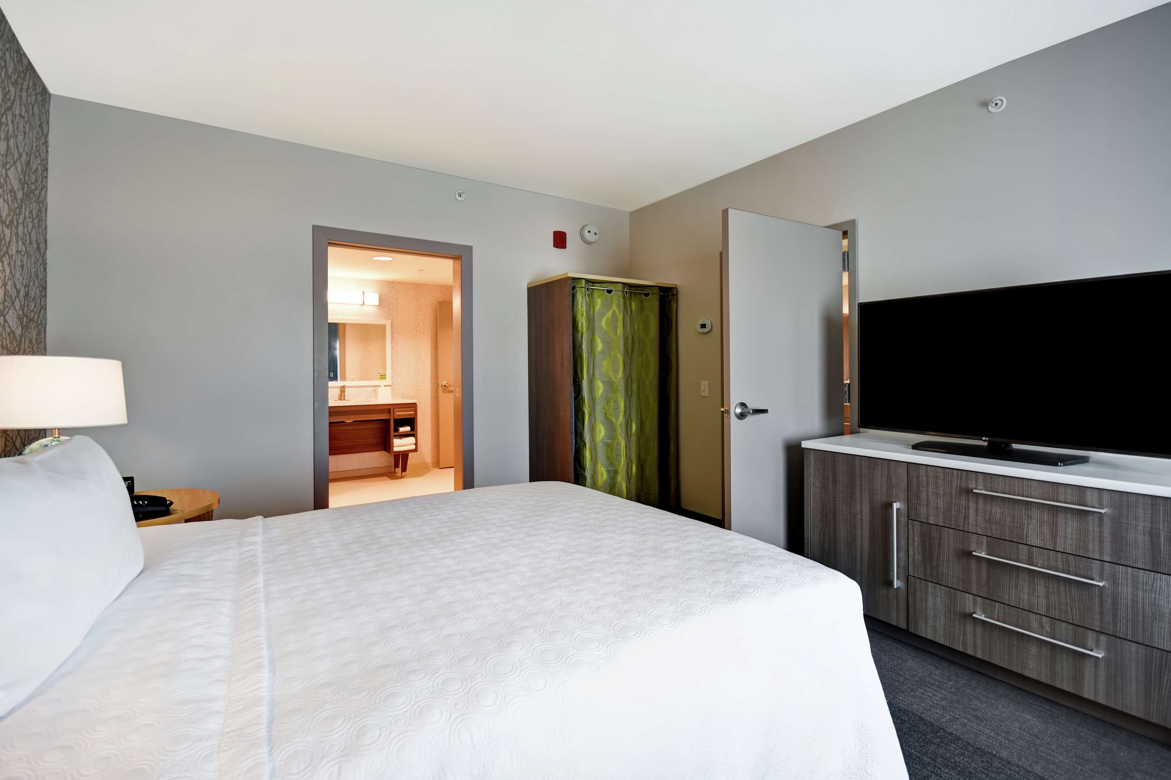 Una habitación de hotel con una cama grande, un televisor sobre un mueble de madera y un baño visible a través de una puerta abierta.