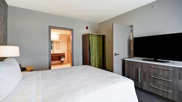 Una habitación de hotel con una cama grande, un televisor sobre un mueble de madera y un baño visible a través de una puerta abierta.
