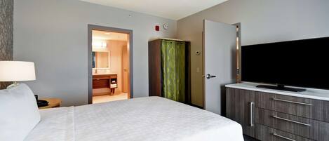 Una habitación de hotel con una cama grande, un televisor sobre un mueble de madera y un baño visible a través de una puerta abierta.