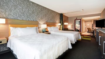 Habitación de hotel con dos camas, televisión, escritorio y baño visible a través de una puerta abierta.