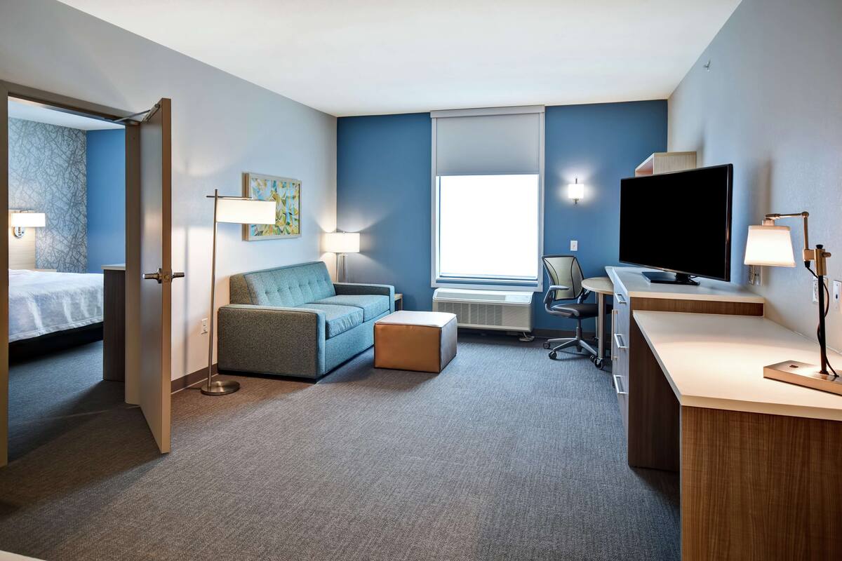 A hotel room with a bed, a sofa, a desk with a TV, and a window.