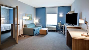 A hotel room with a bed, a sofa, a desk with a TV, and a window.