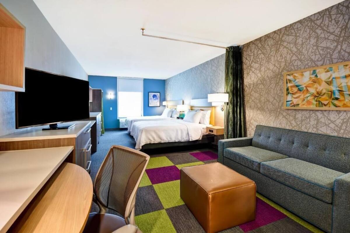 A hotel room with a bed, a sofa, a desk with a TV, and a chair.