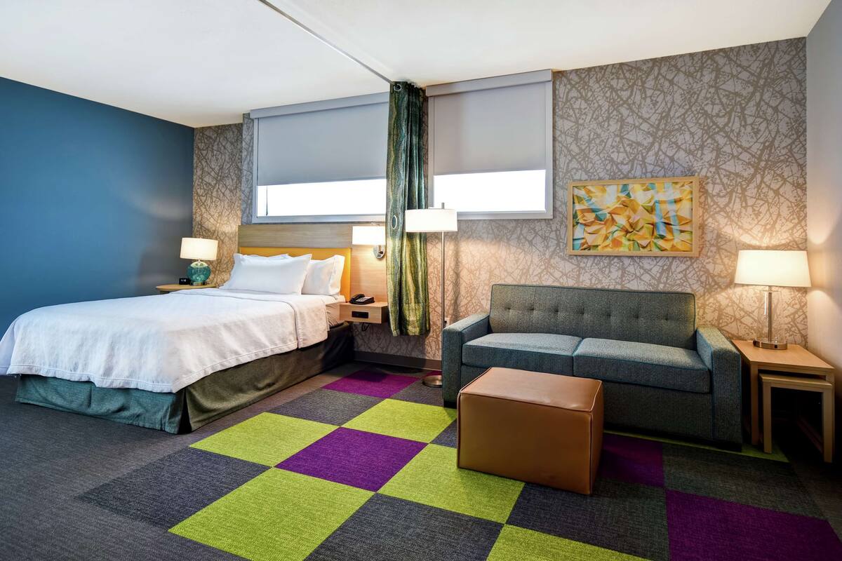 A hotel room with a bed, a sofa, a coffee table, and a patterned rug.