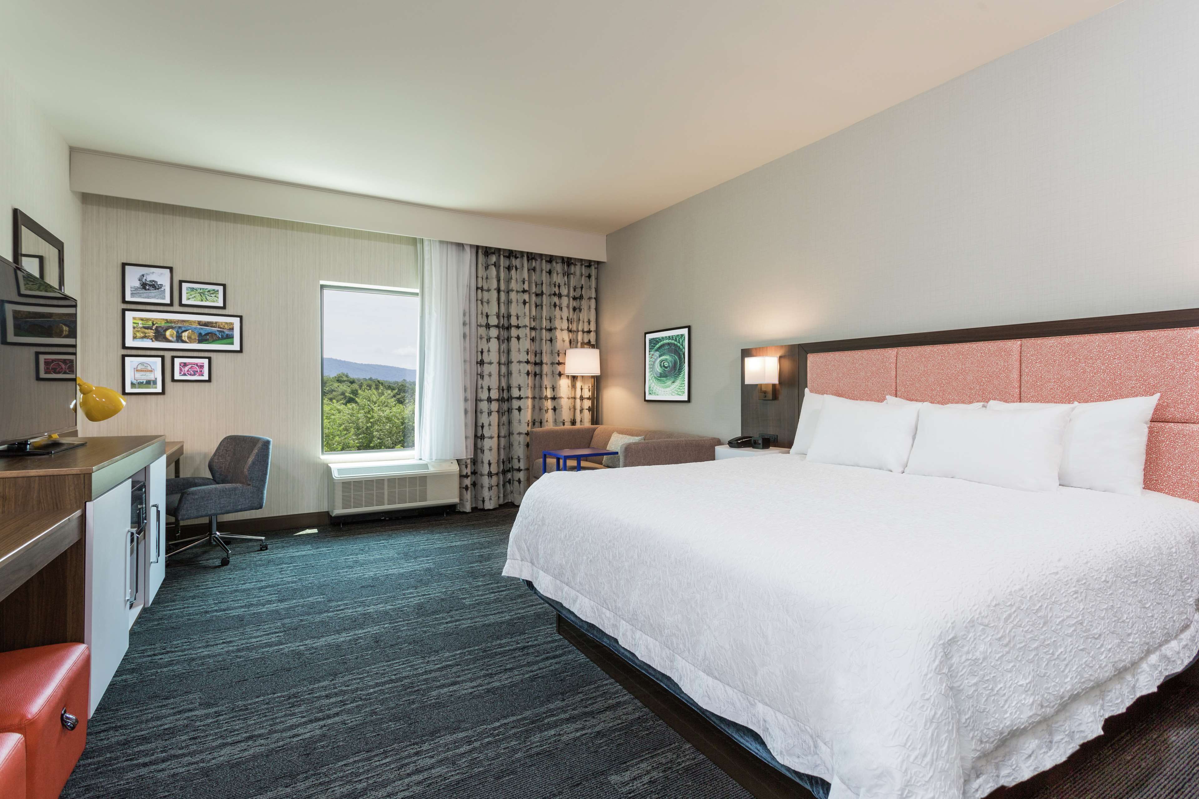 A hotel room with a large bed, a desk with a chair, a small table, and a window with curtains.