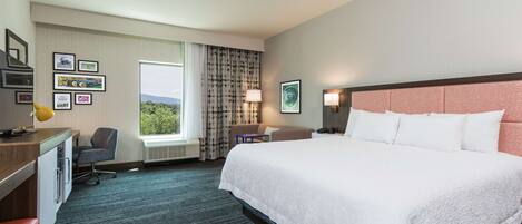 A hotel room with a large bed, a desk with a chair, a small table, and a window with curtains.
