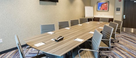Een vergaderzaal met een lange tafel, stoelen, een whiteboard en een televisie aan de muur.