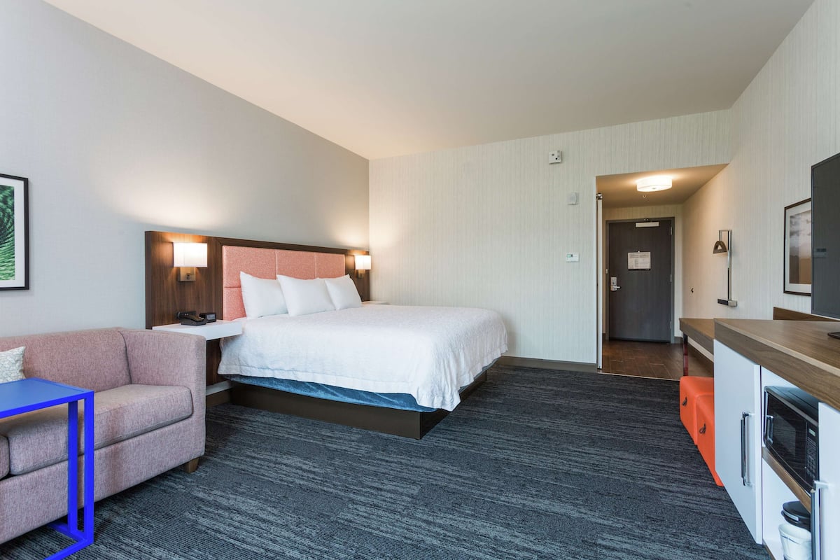 A hotel room with a bed, a desk, a chair, a television, and a kitchenette.
