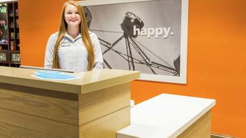 A reception desk with a wooden finish and a white counter. Behind the desk, there is a wall with an orange backdrop and a black and white image of a Ferris wheel with the word "happy."