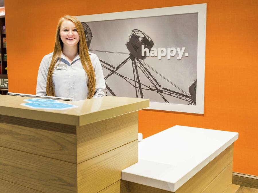A reception desk with a wooden finish and a white counter. Behind the desk, there is a wall with an orange backdrop and a black and white image of a Ferris wheel with the word "happy."