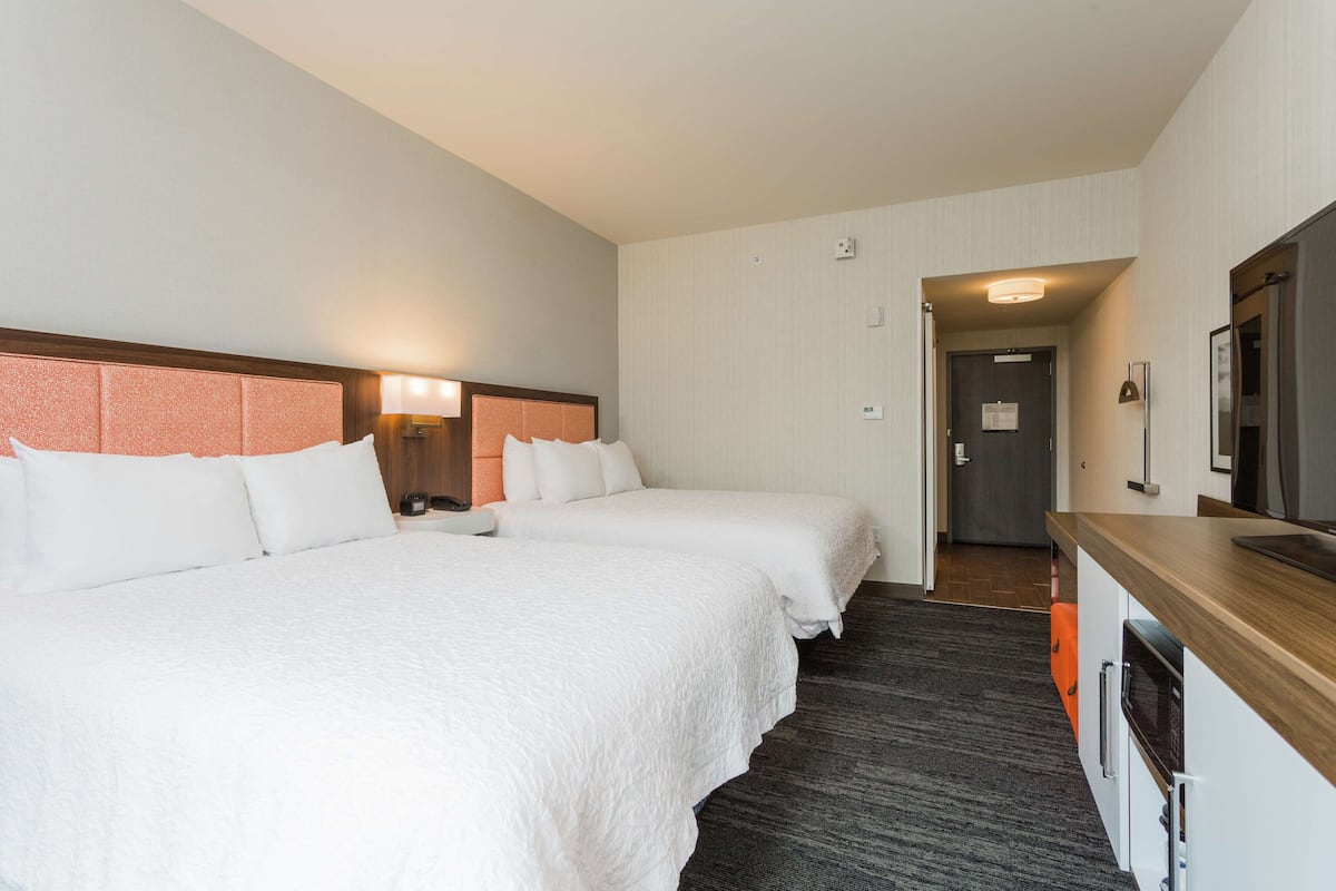 A hotel room with two beds, a wooden desk, and a mirror.