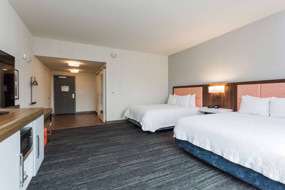 A hotel room with two beds, a kitchenette, and a bathroom.