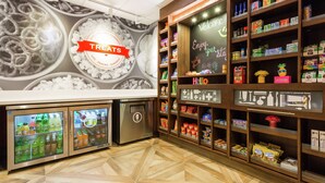 Un bar de aperitivos con un letrero que dice 'TREATS', bebidas refrigeradas y estantes llenos de bocadillos y condimentos.