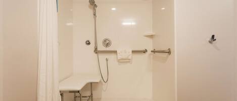 A walk-in shower with a bench, grab bar, and a handheld showerhead.