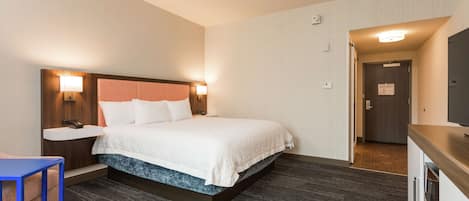 A hotel room with a bed, bedside table, lamp, and a view of the hallway.