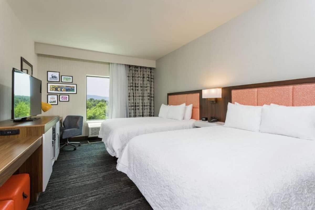 A hotel room with two beds, a desk with a computer, a chair, and a window with curtains.