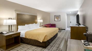 A hotel room with a bed, bedside lamps, a desk with a computer, a television, and a small seating area.