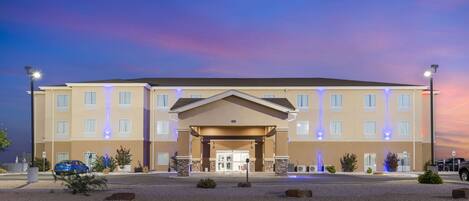 A multi-story hotel with a central entrance, a parking lot, and a clear sky.