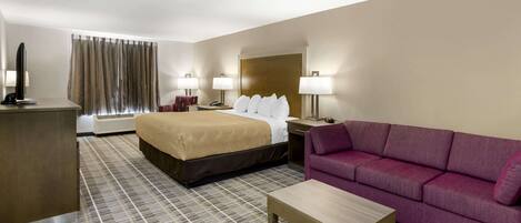 A hotel room with a large bed, a sofa, a desk, and a television.