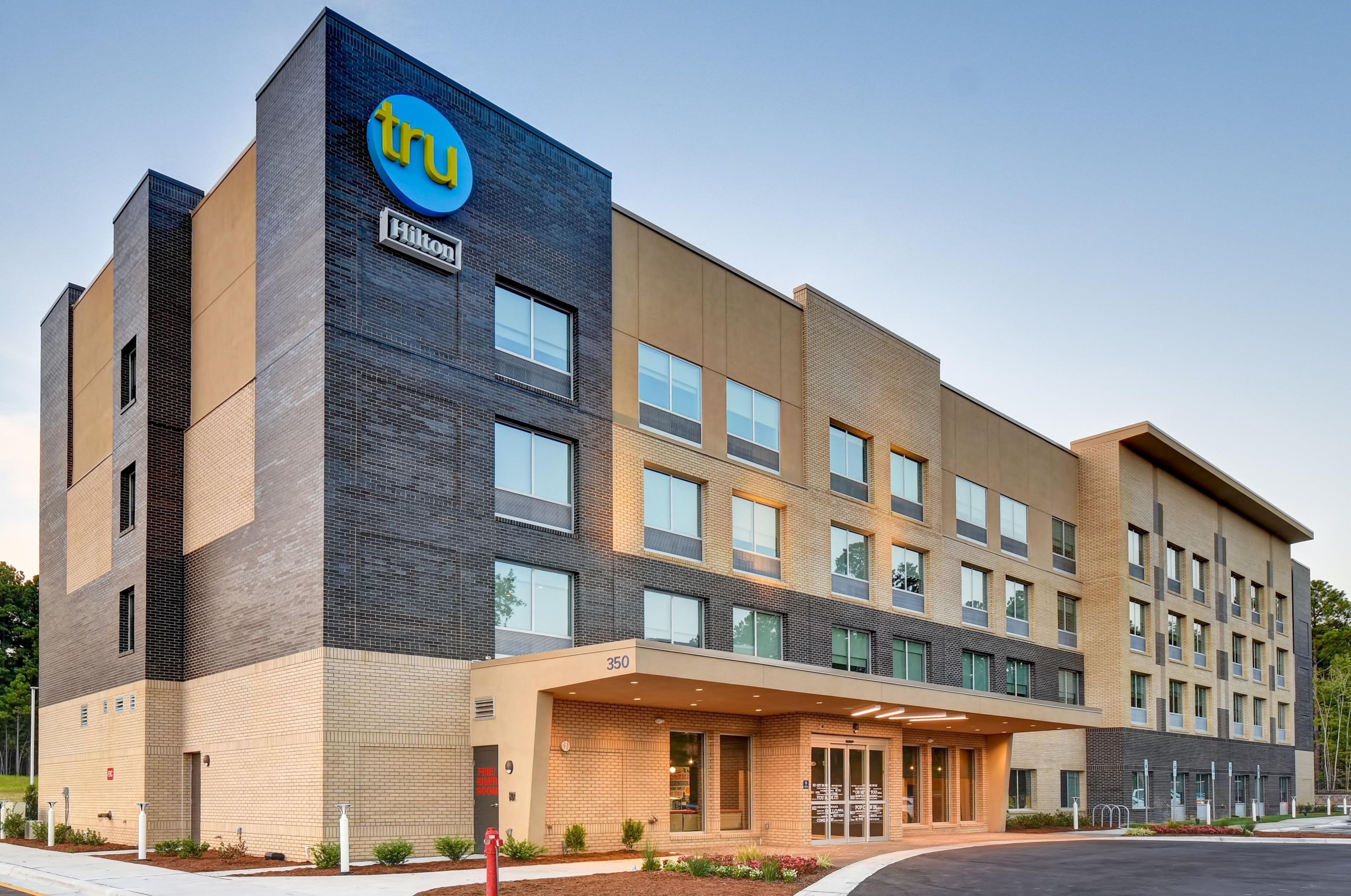 A modern hotel building with a prominent Tru hotel logo, multiple floors, and a covered entrance area.