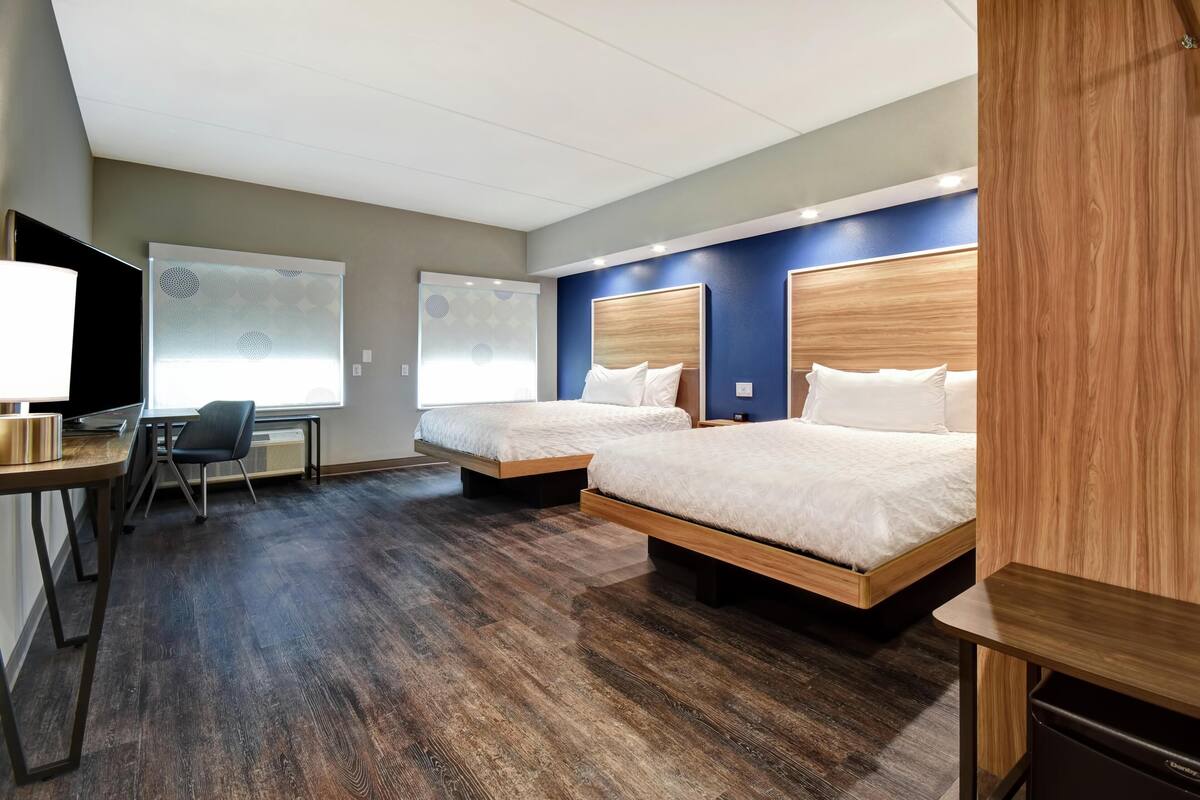 A hotel room with two beds, a desk, a chair, and a TV.