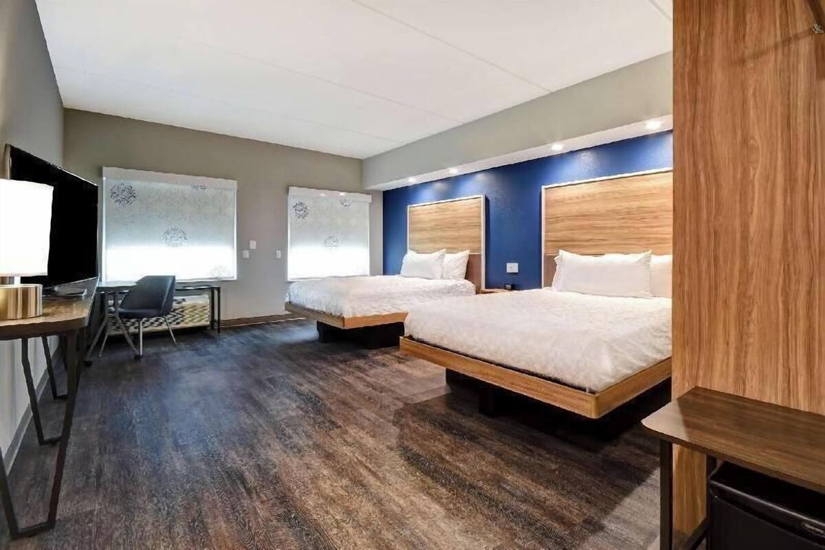A hotel room with two beds, a desk, a chair, and a television.