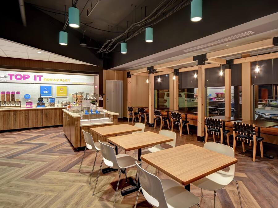 A breakfast area with wooden tables and chairs, a counter with food items, and a view of the outside.