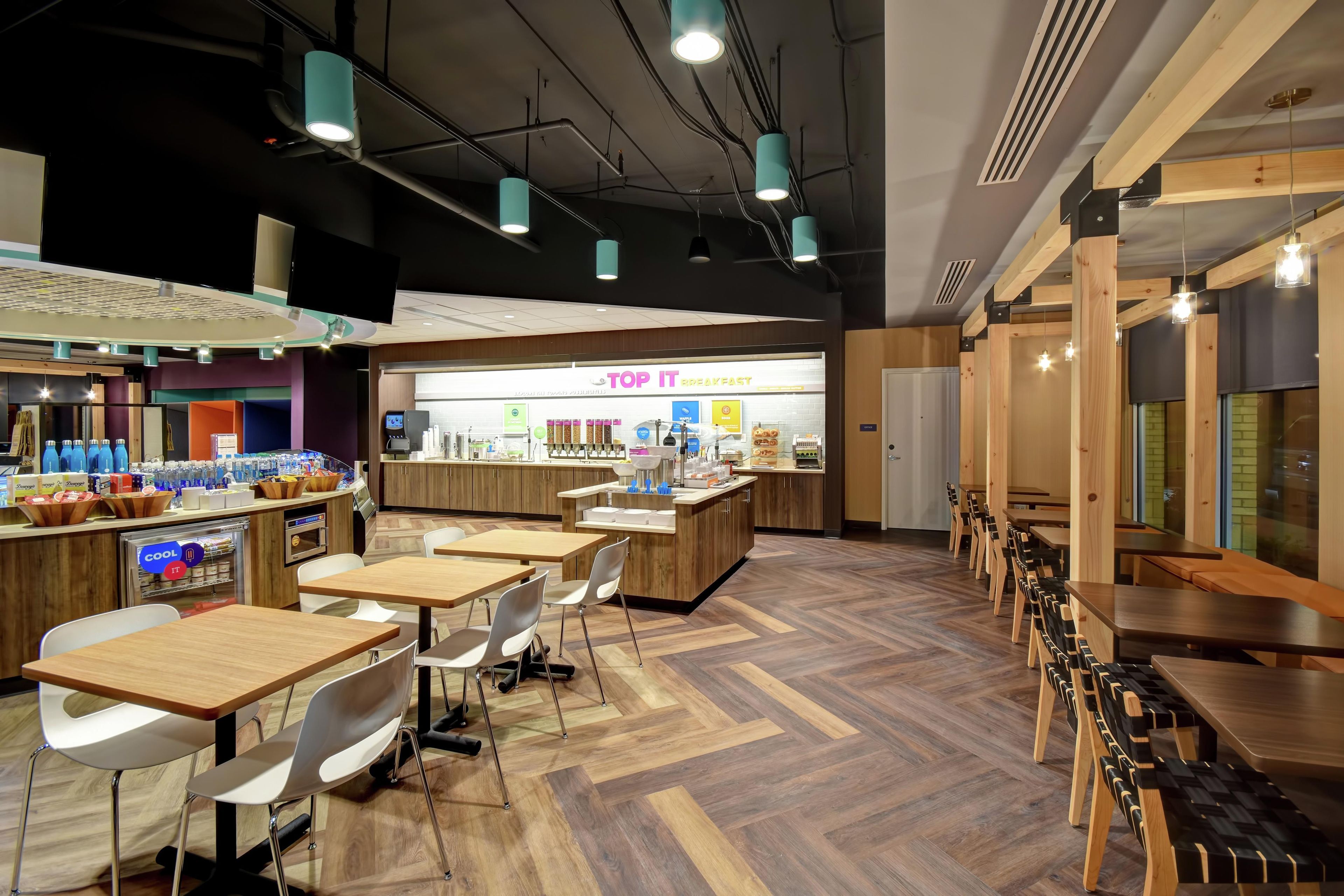 A modern cafe with wooden tables and chairs, a visible counter with a menu, and a herringbone-patterned floor.