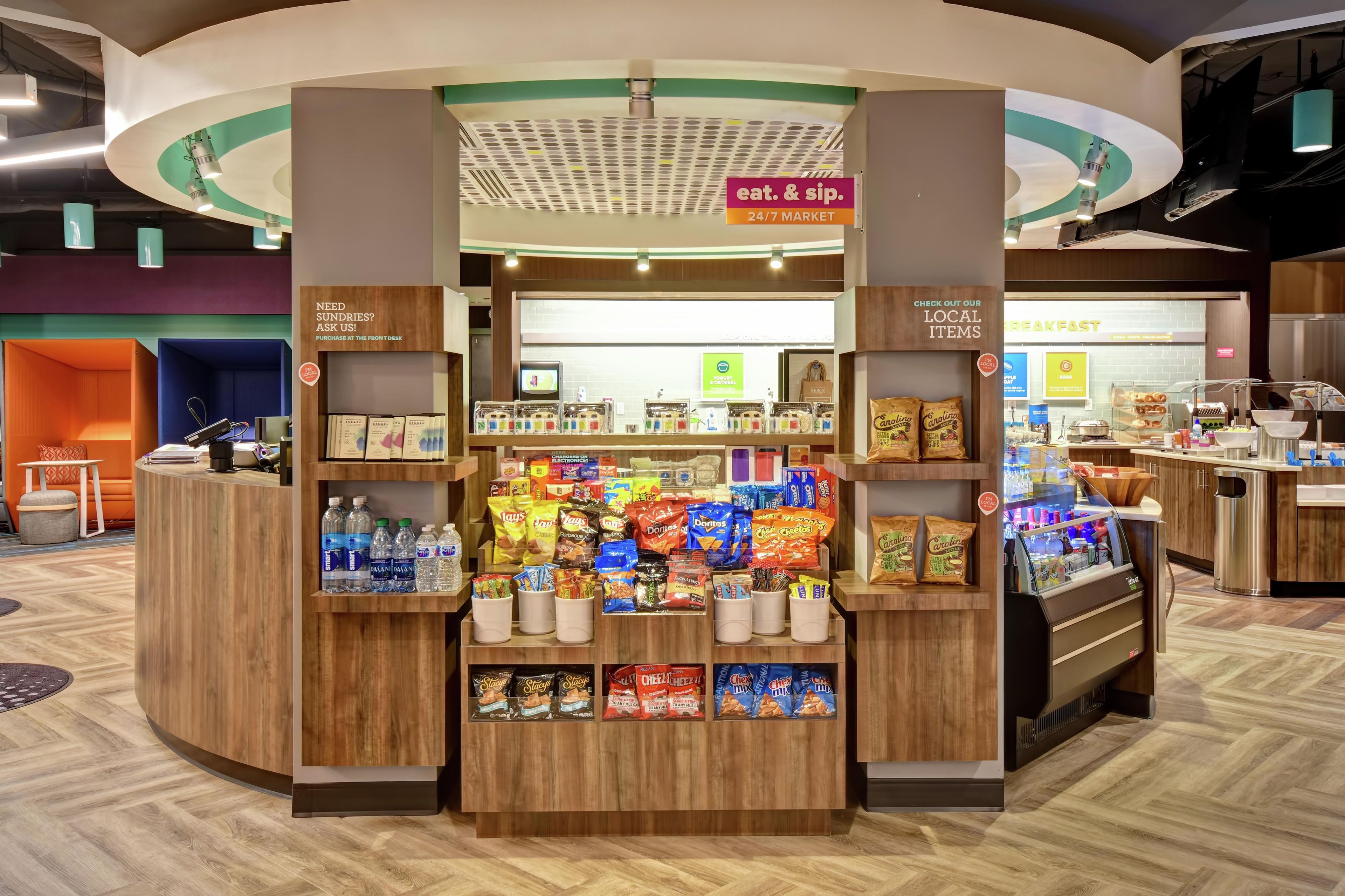 Un marché ouvert 24 heures sur 24, 7 jours sur 7, proposant une variété de collations et de boissons, un espace pour prendre le petit-déjeuner, et une enseigne indiquant l’emplacement d’une boutique de produits locaux.