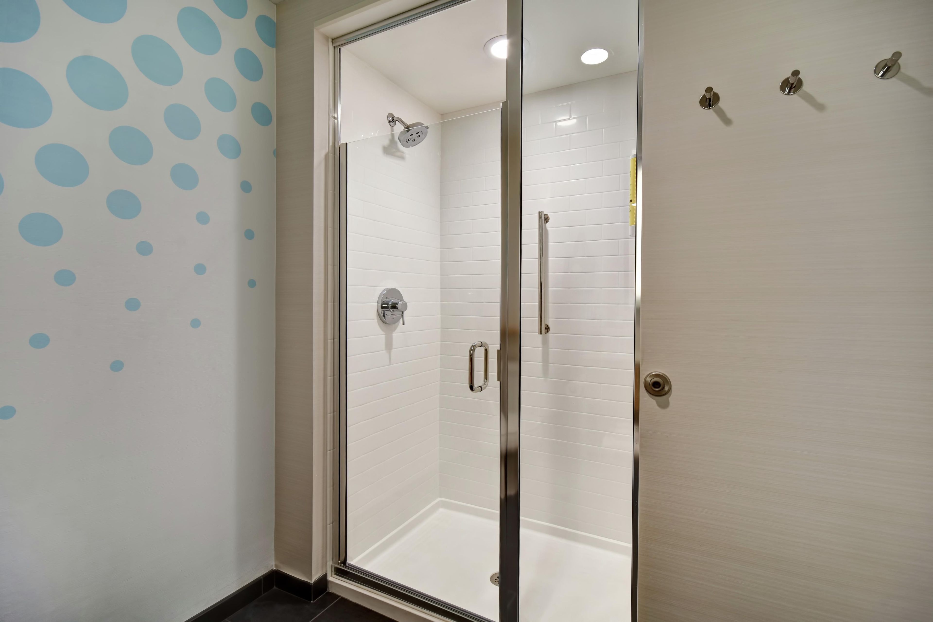 A glass-enclosed shower with a handheld showerhead, a wall-mounted towel rack, and a door with a metallic handle.