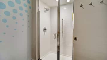 A glass-enclosed shower with a handheld showerhead, a wall-mounted towel rack, and a door with a metallic handle.