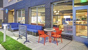 An outdoor seating area with a blue sofa, orange chairs, and a table. - Tru by Hilton Raleigh Durham Airport (Morrisville)