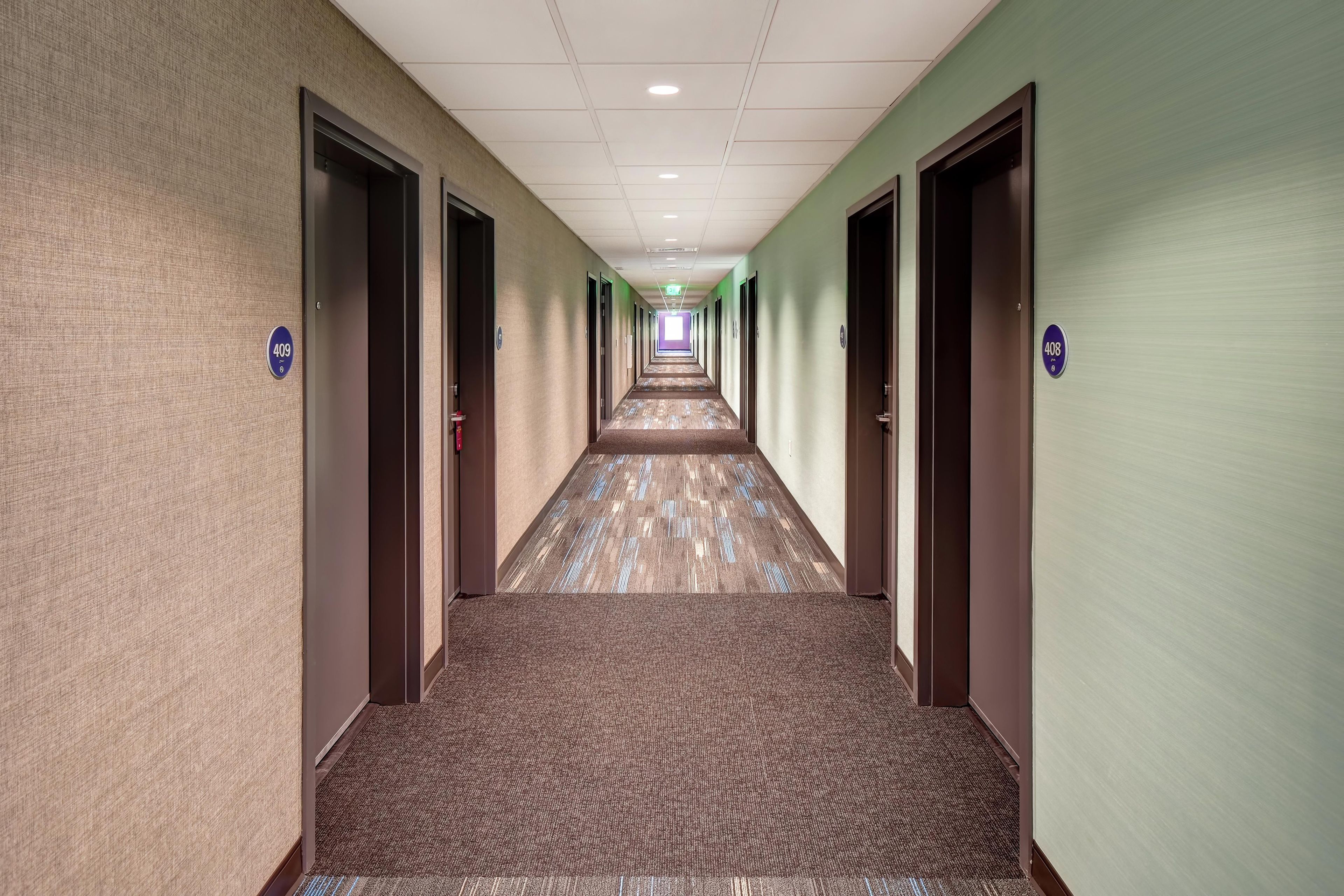Un pasillo de hotel con piso alfombrado, puertas con números de habitación e iluminación empotrada en el techo.