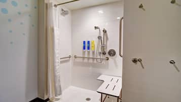 Une douche à l’italienne avec un mur recouvert de carreaux blancs, un pommeau de douche fixe, un pommeau de douche amovible, un panneau de commande de la douche et un lavabo blanc avec un cadre en métal.