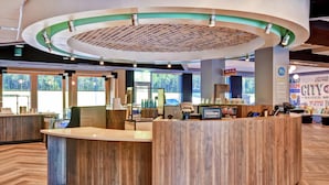 A hotel reception area with a wooden reception desk, large windows, and a circular ceiling design. - Tru by Hilton Raleigh Durham Airport (Morrisville)