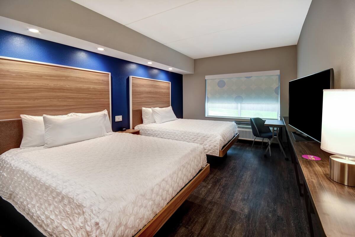 A hotel room with two beds, a desk, a chair, a TV, and a window with a view.