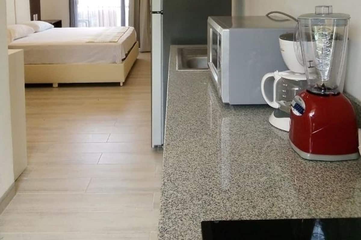 Habitación de hotel pequeña con cama, kitchenette y una licuadora roja sobre la encimera.